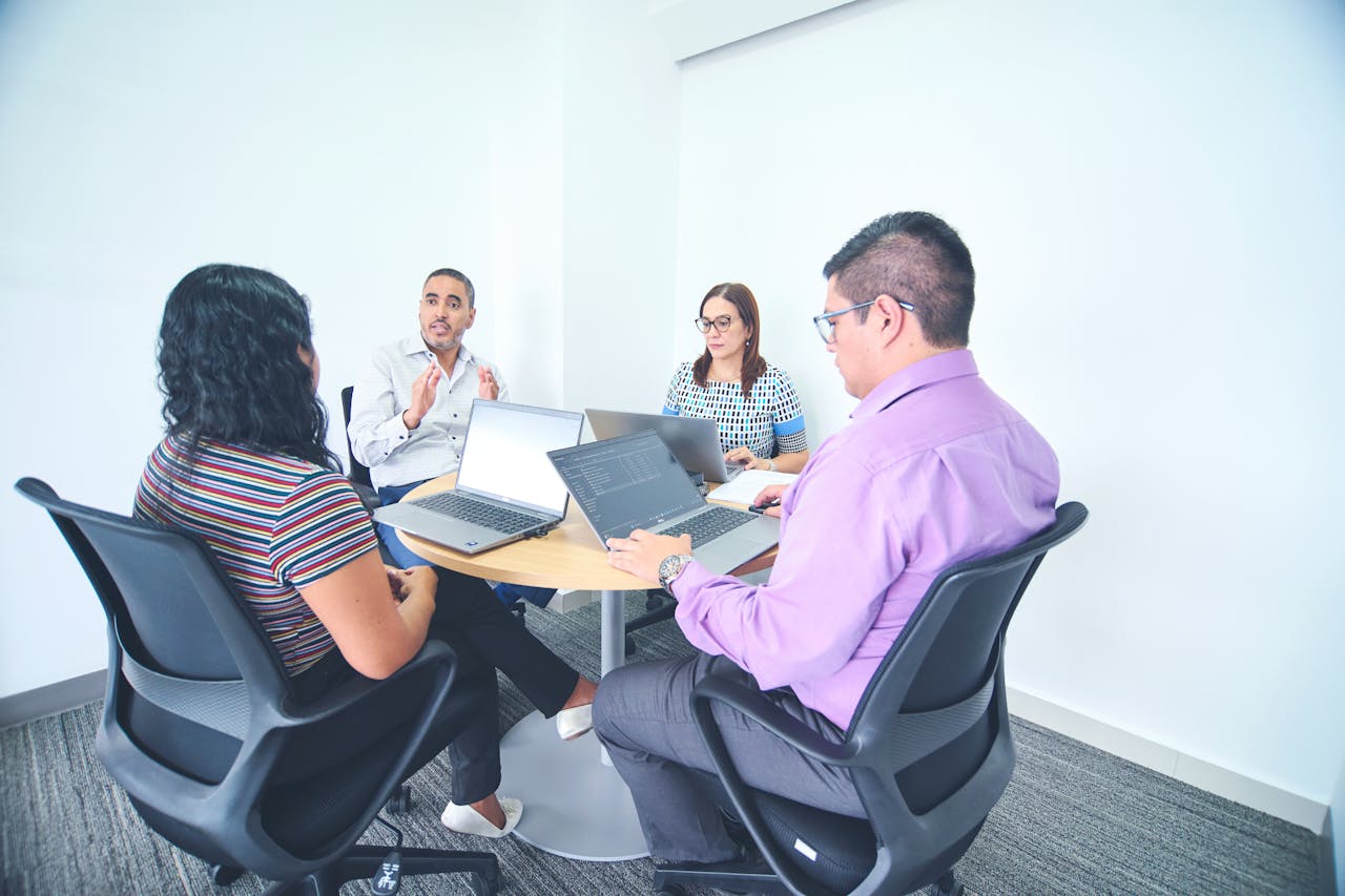Diverse team engaged in a corporate meeting with laptops in a bright, modern office setting.